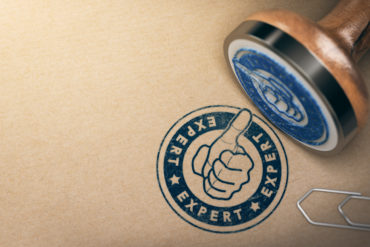 Wooden Rubber Stanp over brown cardboard background with the text expert printed in blue color. Concept of professional advice and industrial expertise. 3D illustration